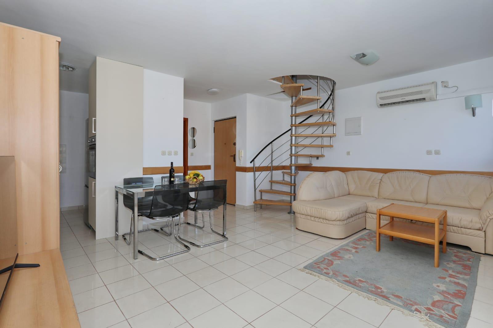 Apartman Gumbek — dnevni boravak s blagovaonskim stolom i spiralnim stubištem na gornju etažu