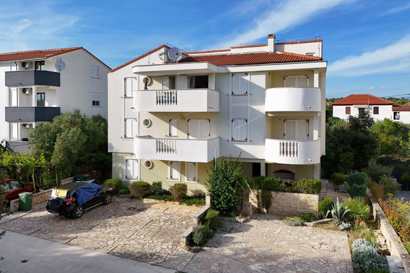 Zgrada s apartmanima Mare i Gumbek u Petrčanima — bijela fasada, balkoni i parkirno dvorište